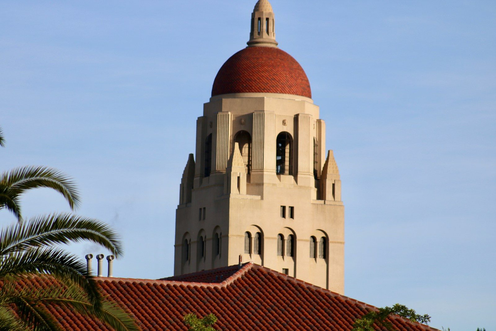 Hoover Tower rising above Stanford University campus with palm trees and blue sky